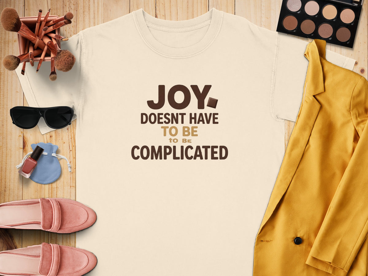 Cream t-shirt with "JOY DOESN'T HAVE TO BE COMPLICATED" text, styled with makeup and clothing.