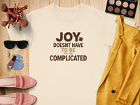 Cream t-shirt with "JOY DOESN'T HAVE TO BE COMPLICATED" text, styled with makeup and clothing.