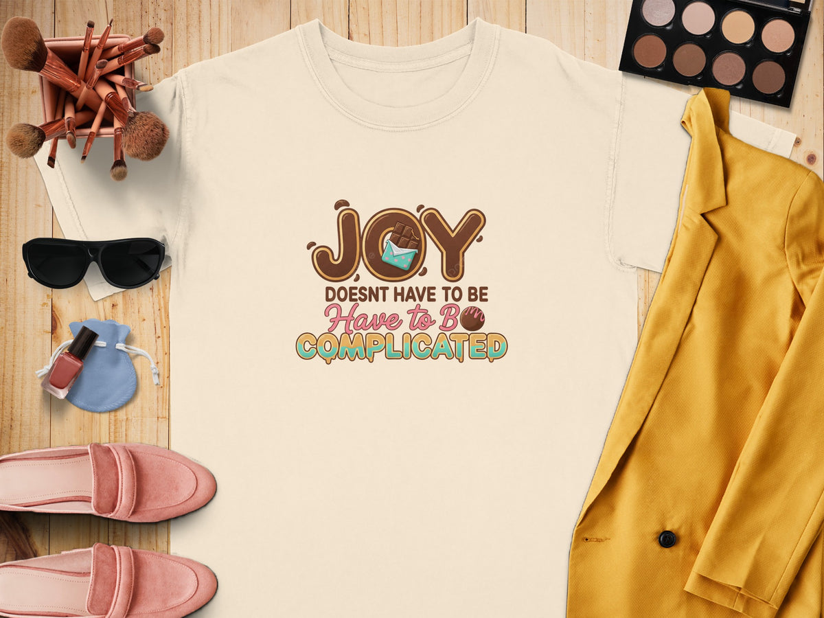 Cream t-shirt with "JOY DOESN'T HAVE TO BE COMPLICATED" text and chocolate detail.