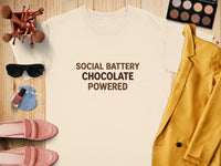 Cream t-shirt with "SOCIAL BATTERY CHOCOLATE POWERED" text, surrounded by makeup and clothing.