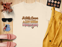 Light yellow t-shirt with "A Little Cocoa A LOT MORE Human" text and heart graphic.