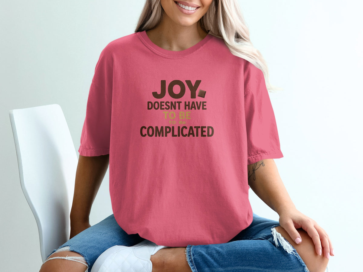 Pink t-shirt with dark brown text: "JOY DOESN'T HAVE TO BE COMPLICATED."